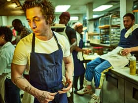 Jeremy Allen White as Carmen ‘Carmy’ Berzatto in The Bear, wearing a blue apron, holdin a spoon in a restaurant kitchen (Credit: Frank Ockenfels/FX )