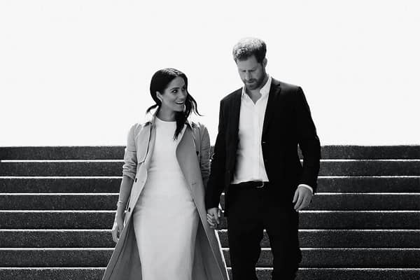 A black and white image of Meghan Markle and Prince Harry walking down a flight of stairs together, hand in hand and smiling (Credit: Netflix) 