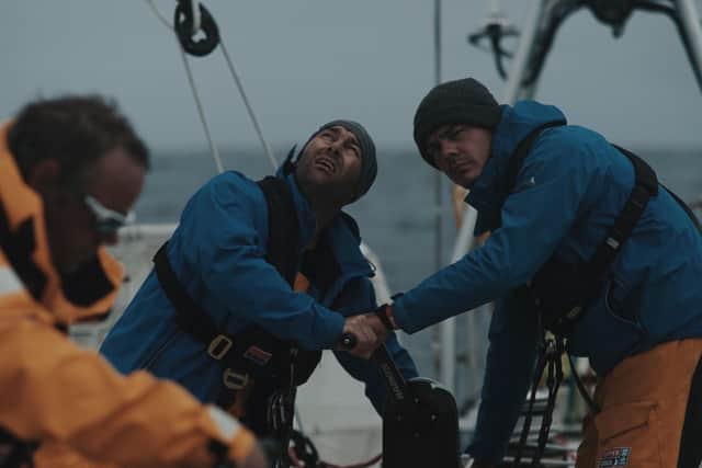 Olly (right) uses the 'coffee grinder' to adjust the sails on board with teammates