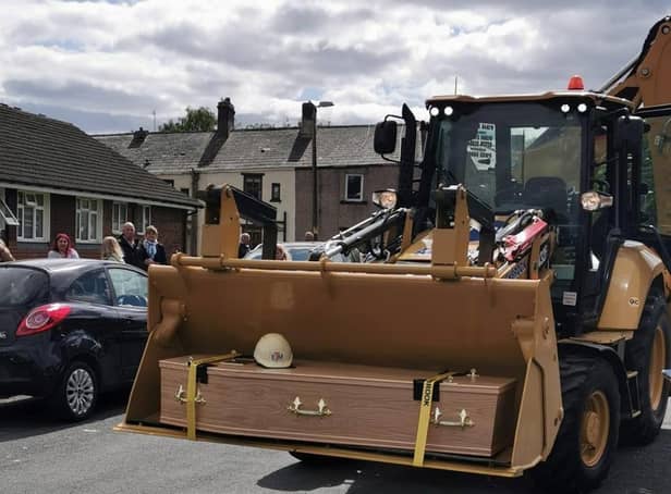The coffin of Padiham man Roy Mellor is placed into the cradle of the JCB, poignantly topped with a hard hat.