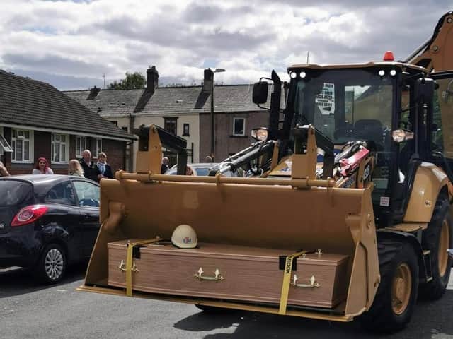 The coffin of Padiham man Roy Mellor is placed into the cradle of the JCB, poignantly topped with a hard hat.