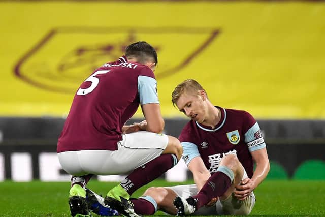 Ben Mee of Burnley lies injured and is checked on by teammate James Tarkowski during the Premier League match between Burnley and Wolverhampton Wanderers at Turf Moor on December 21, 2020 in Burnley, England.