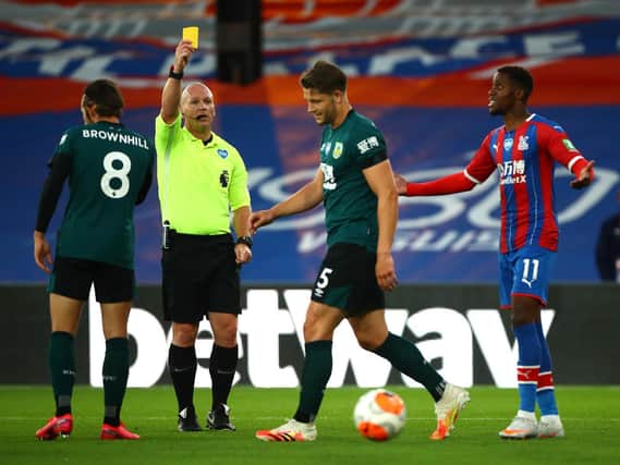James Tarkowski of Burnley is shown a yellow card by referee Simon Hooper as Wilfried Zaha of Crystal Palace reacts during the Premier League match between Crystal Palace and Burnley FC at Selhurst Park on June 29, 2020 in London, United Kingdom.