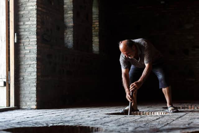 A winemaker looks over his red wine, fermenting in a qvervi buried in the soil of a winery. Picture: Miles WIllis