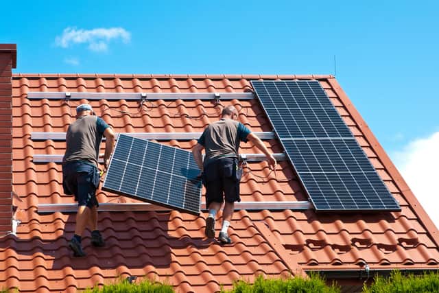 Two men installing new solar panels on the roof of a private house. Photo: Adobe