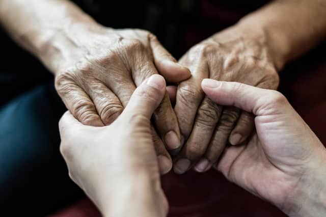 Female senior elderly patient with Parkinson's and Alzheimer's holding hands with her carer.