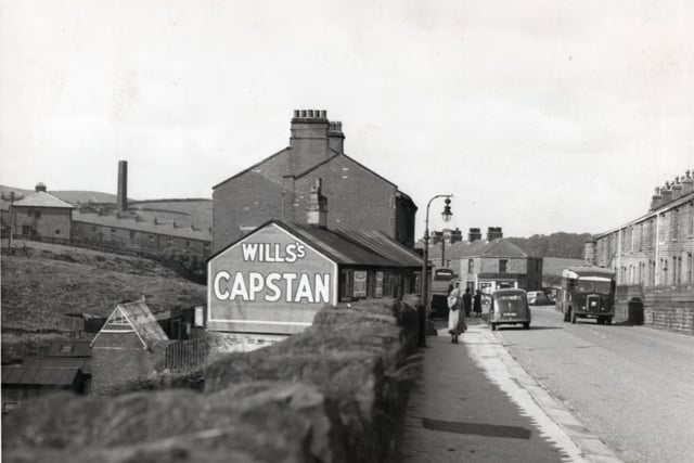 The Burnley Road in Walk Mill showing two of the shops in the village. The one on the right, a grocer’s and, at one time the Post Office, has a huge advert for Will’s Capstan cigarettes on the gable end. The top of the village telephone box can be seen nearby. On the extreme left the chimney to the Cliviger Colliery can be seen. On the right is one of the two long terraces of houses on the roadside. Longfield Terrace can be seen, left.
