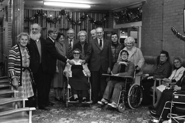 Mr Hall (third from the left) receives the cheque from Coun. Pickup. Looking on are Temple Street centre users and Mrs B. Thornber (centre manager, fourth from left), Mr Jack Peel (manager, day care services, fifth from left), members of staff and Mrs J. Pickup (standing behind the new wheelchair on the right).
Coun. Albert Pickup, who was Burnley's Mayor in 1978-79, closed his charity fund with two final donations - to the Temple Street Centre and to Express Help.