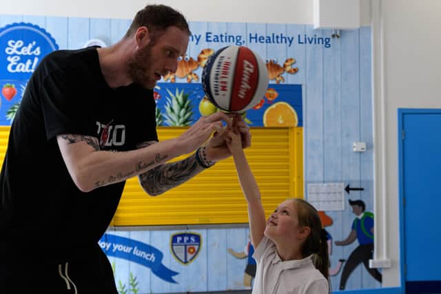 The tallest man in the UK Paul Sturgess shows off his basketball skills by balancing the ball on a pupils hand. Photo: Kelvin Stuttard