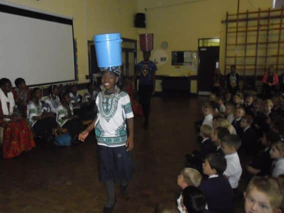 A member of the Bethany Choir demonstrates how to carry a bucket of water on her head to children at St Mary Magdalene's RC Primary School in Burnley ((s)