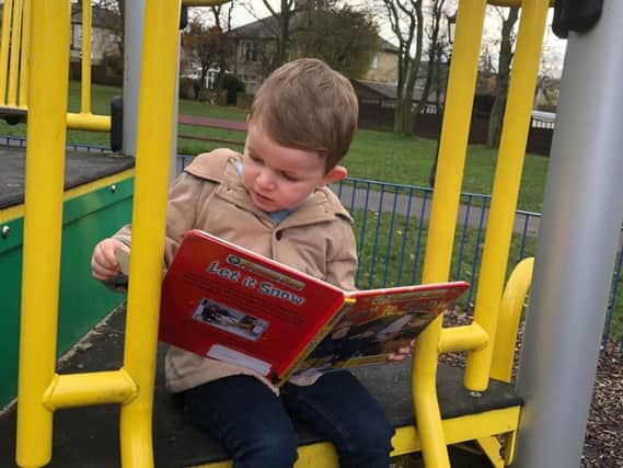 Myles Caldecott (two) is engrossed in the book he chose from the Ightenhill little free library.