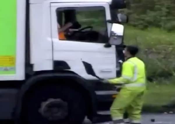 The man from the smaller lorry smashes the window of the big lorry with a spade